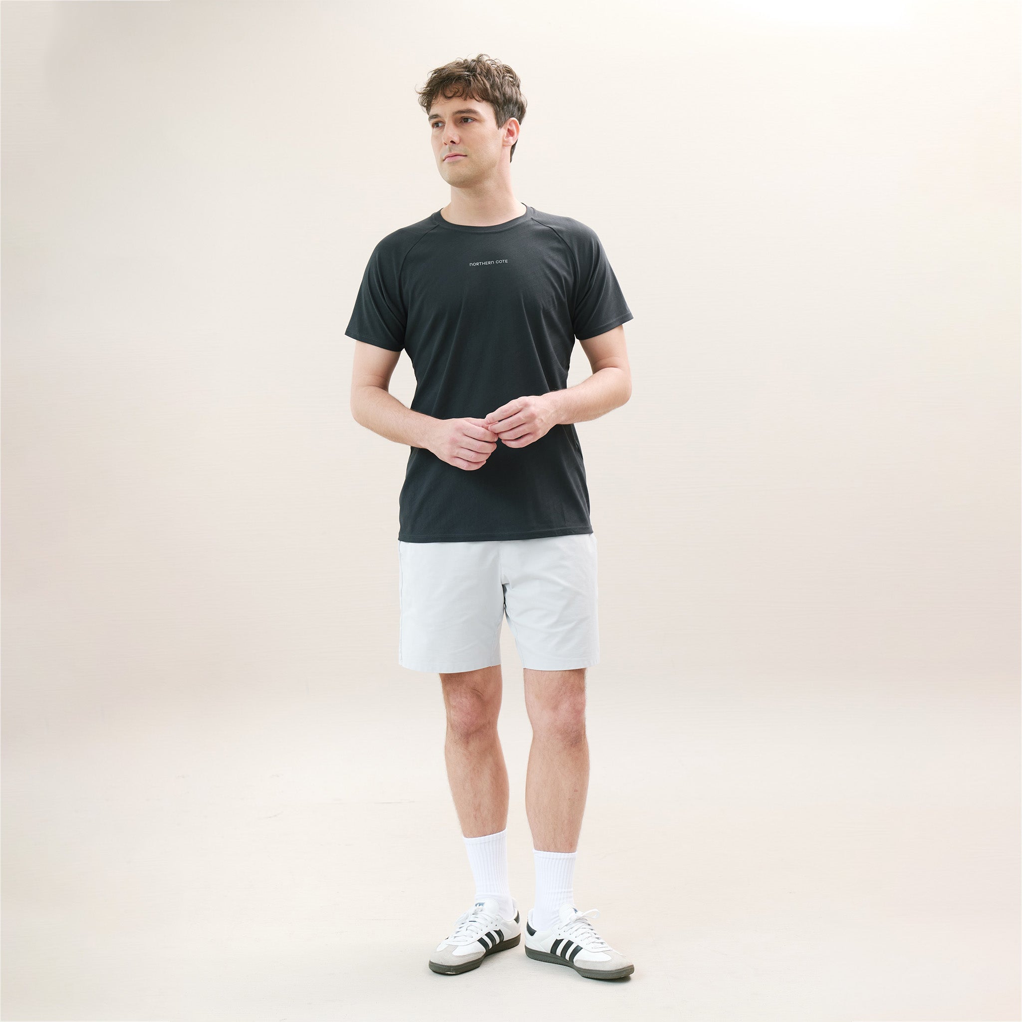 Man wearing a black t-shirt, white shorts, and white sneakers on a plain background