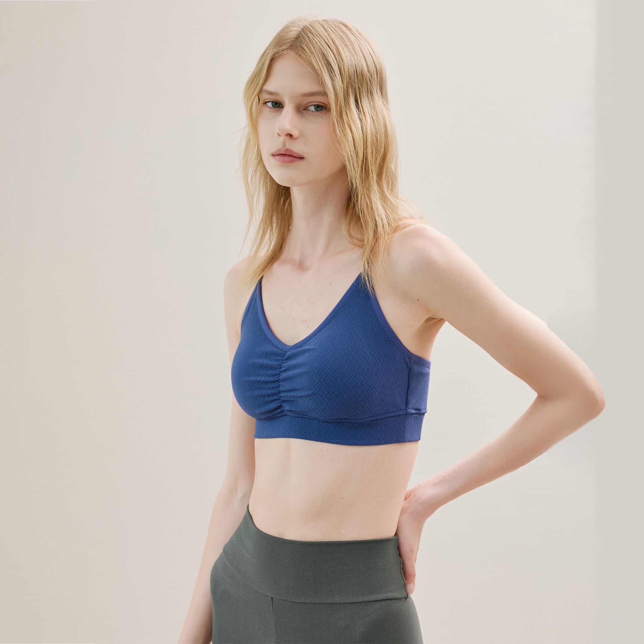 Woman wearing a blue sports bra and gray leggings on a plain background