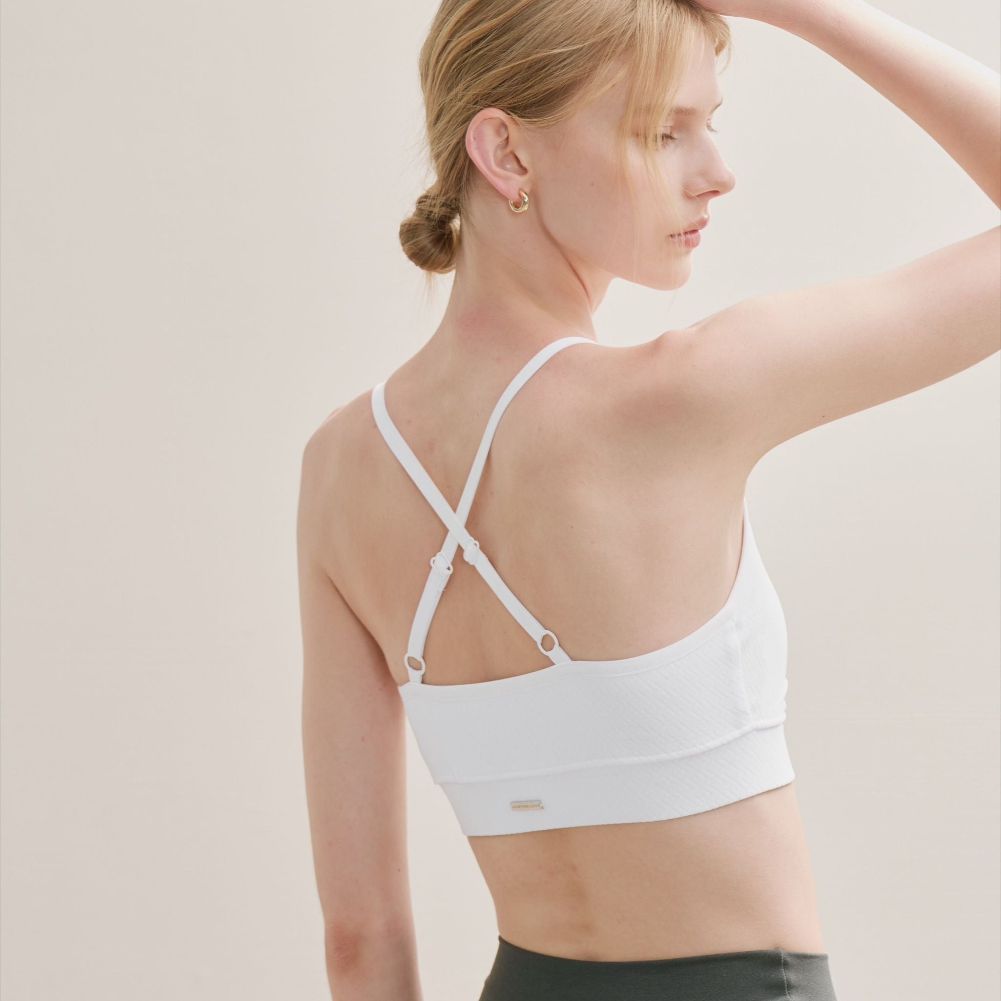 Woman wearing a white sports bra with a neutral background.