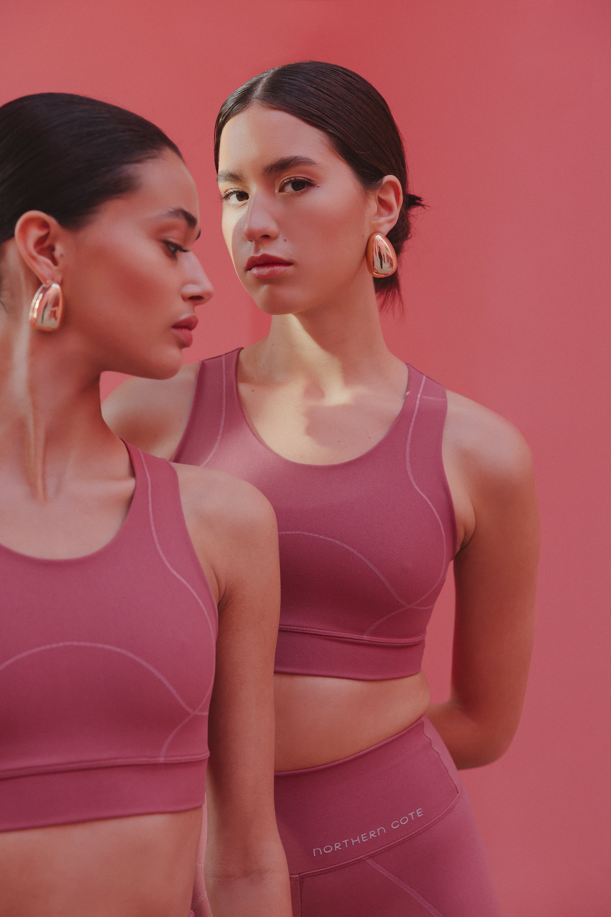 Two models posing side by side in Northern Cote's mauve activewear sets, featuring seamless crop tops and high-waisted leggings, against a pink background.