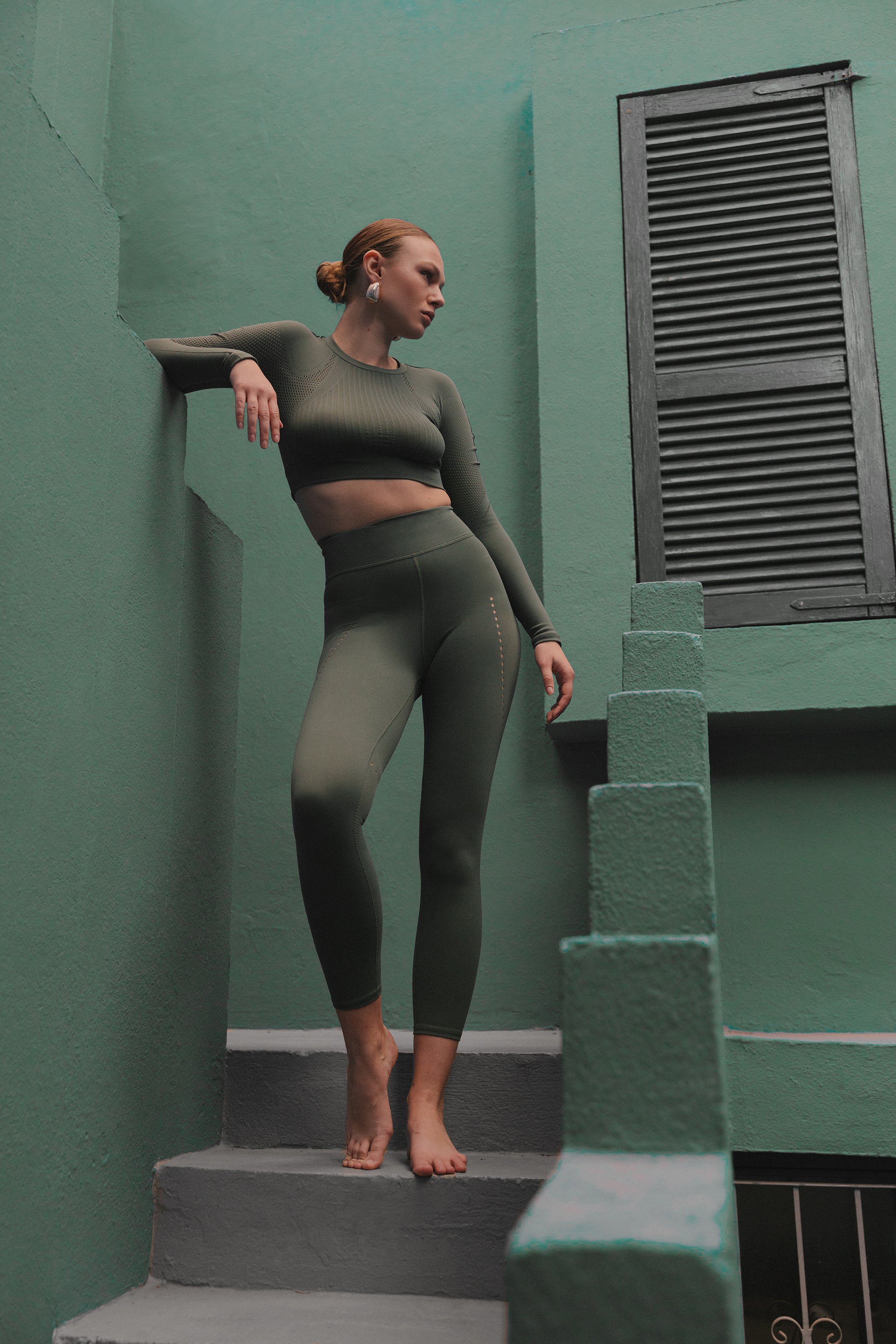 A woman in green activewear poses confidently on the steps of a teal and green stairway, showcasing a blend of fitness and architecture.