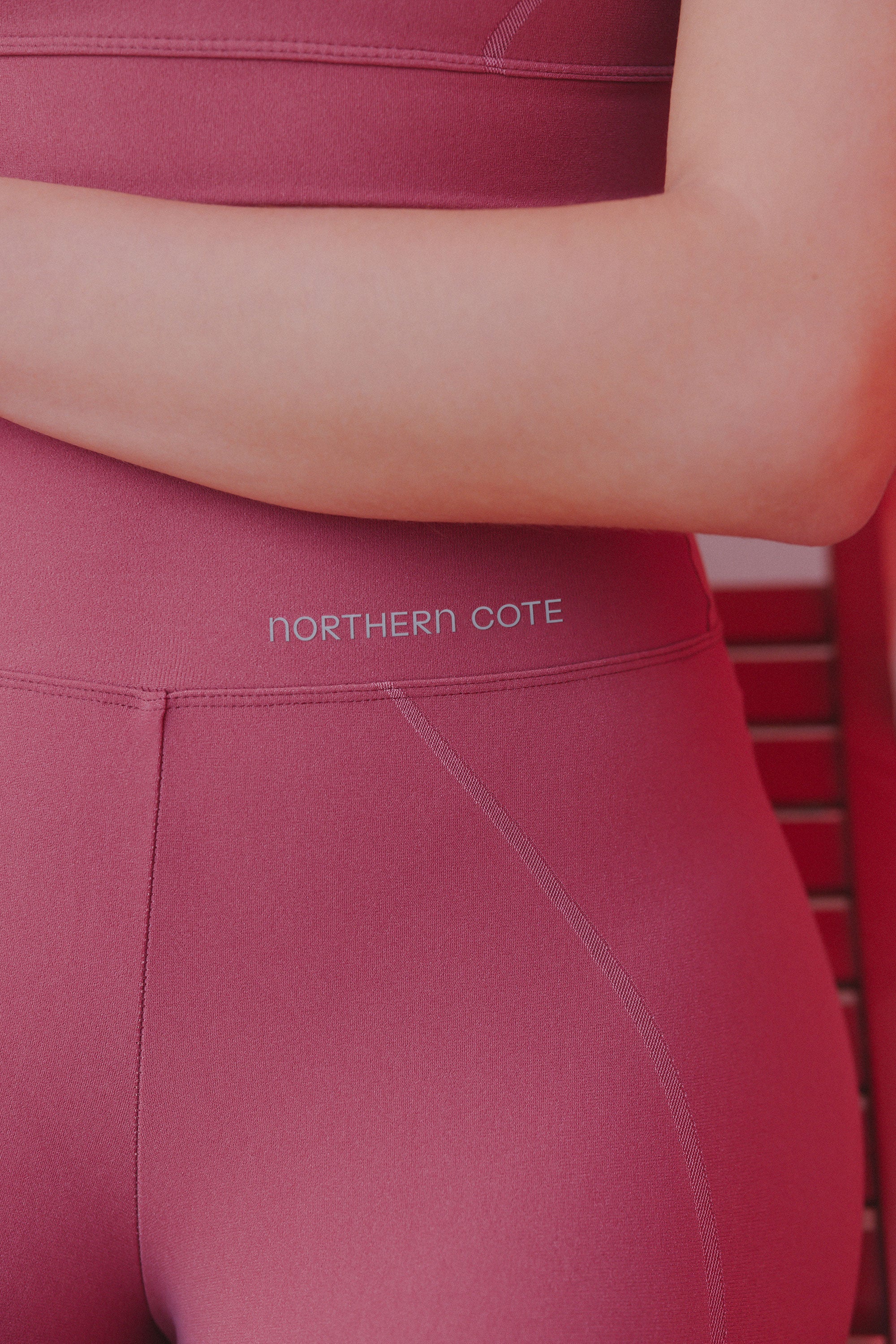 Close-up of a woman's midsection showing a high-waisted burgundy legging with a white brand logo "NORTHERN COTE" around the waistband.