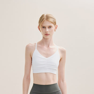Woman wearing a white sports bra and gray leggings on a neutral background