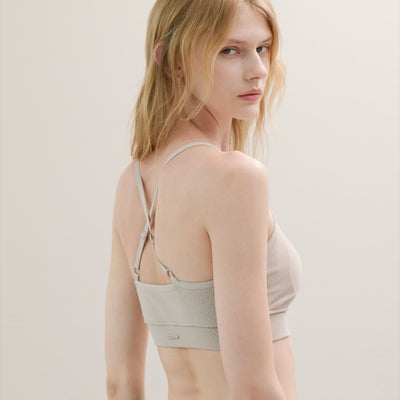 Woman wearing a light-colored bralette against a plain background